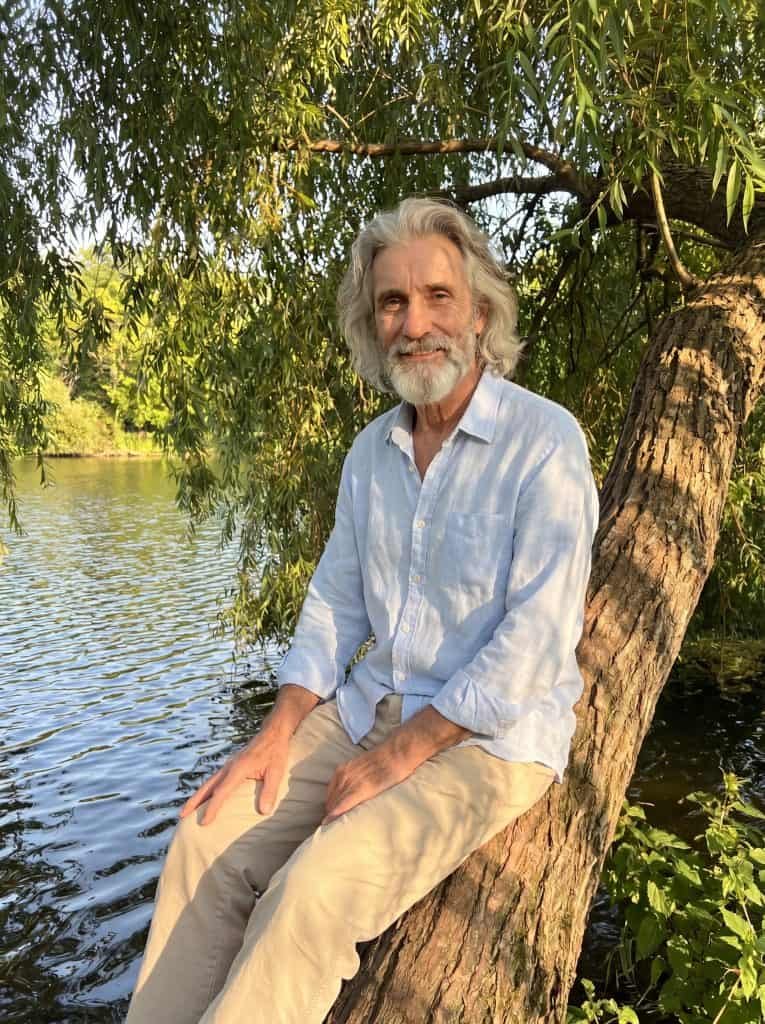 Michael Hartman sitting on large tree by water.